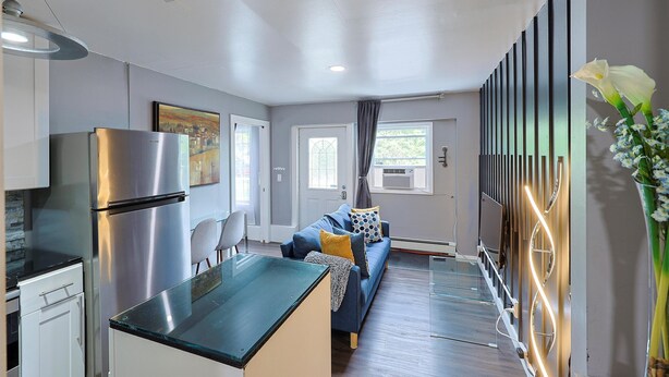 A modern kitchen with a stainless steel refrigerator, a glass-top dining table, and a built-in oven. There is a seating area with a blue sofa and a small table. - Stylish and Pet-Friendly Apartment in Beacon (Beacon)