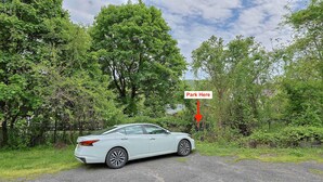 A white car parked on a gravel road with a sign indicating a parking area. - Stylish and Pet-Friendly Apartment in Beacon (Beacon)