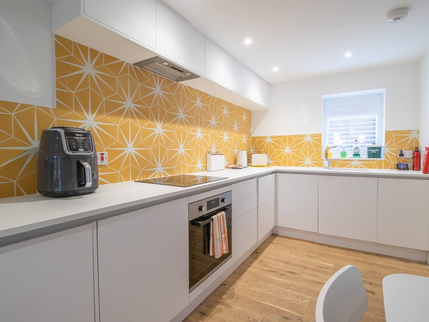 A modern kitchen with a geometric backsplash, a built-in oven, and a coffee maker.
