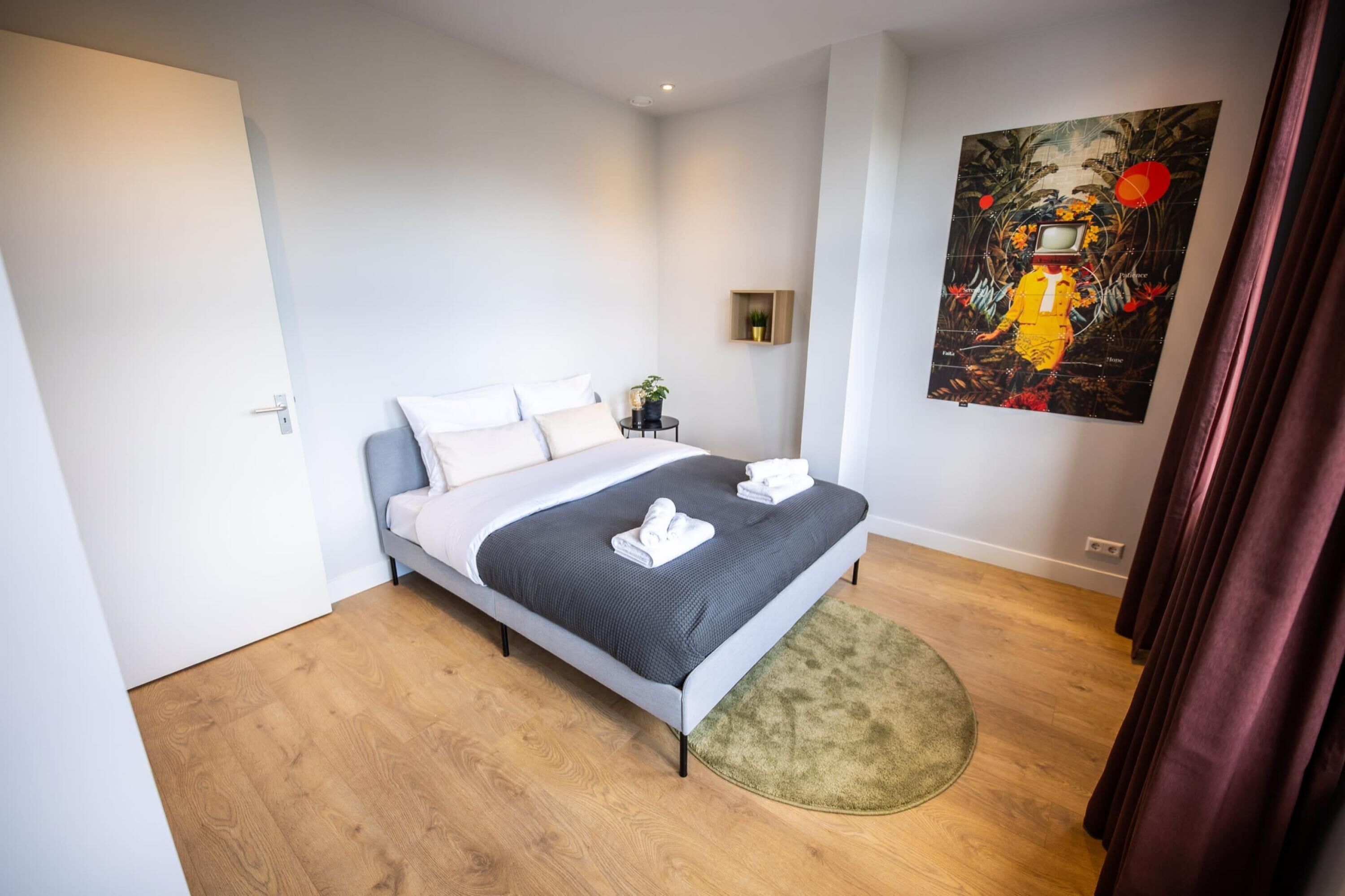A modern bedroom with a bed, a small bedside table, a wall-mounted TV, and a painting.