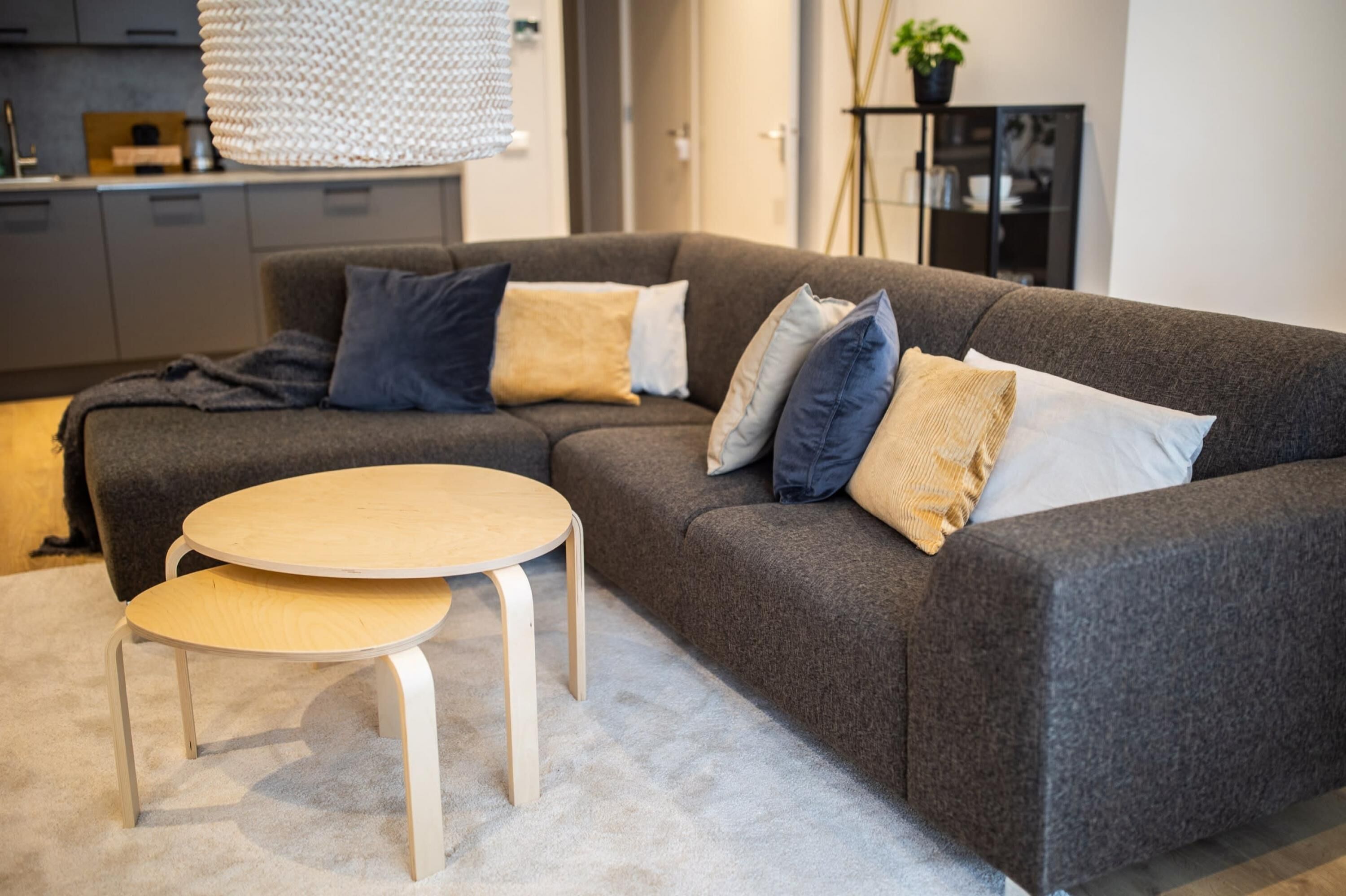 A modern living room with a grey sofa, a round wooden coffee table, and a small side table.