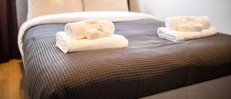 A neatly made bed with a brown textured bedspread and two rolled white towels placed on the footboard.