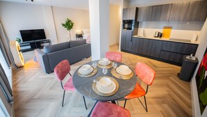 Una sala de estar moderna con un sofá, una mesa de comedor con platos y vasos, y una zona de cocina con armarios y electrodomésticos.