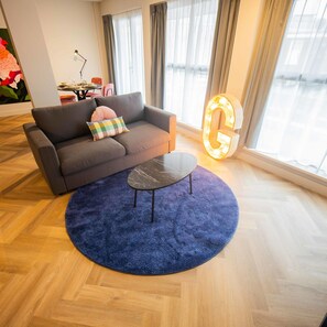 Ett modernt vardagsrum med en grå soffa, en mönstrad kudde, ett runt soffbord och en stor, upplyst bokstav "G".
