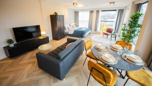 Een moderne woonkamer met een bank, televisie en een eetgedeelte met stoelen en een tafel gedekt voor twee personen.