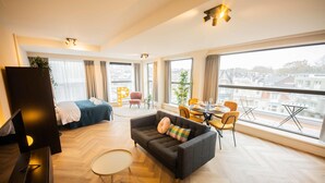 Een moderne hotelkamer met een groot bed, een bank, een eethoek en uitzicht op de stad.