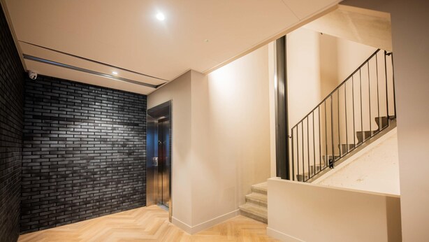 Een modern interieur met een visgraat parketvloer, een muur van zwart baksteen en een trap met een metalen leuning.