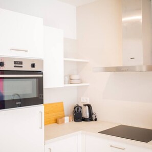 A modern kitchen with white cabinetry, a built-in oven, a stainless steel range hood, and a coffee maker on the countertop.