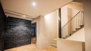 Un interior moderno con suelo de madera en espiga, pared de ladrillo negro y escalera con barandilla de metal.