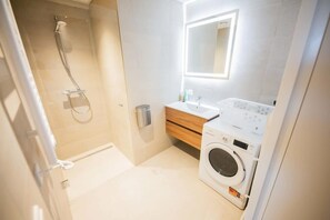 Un baño moderno con ducha, lavabo, espejo y lavadora.