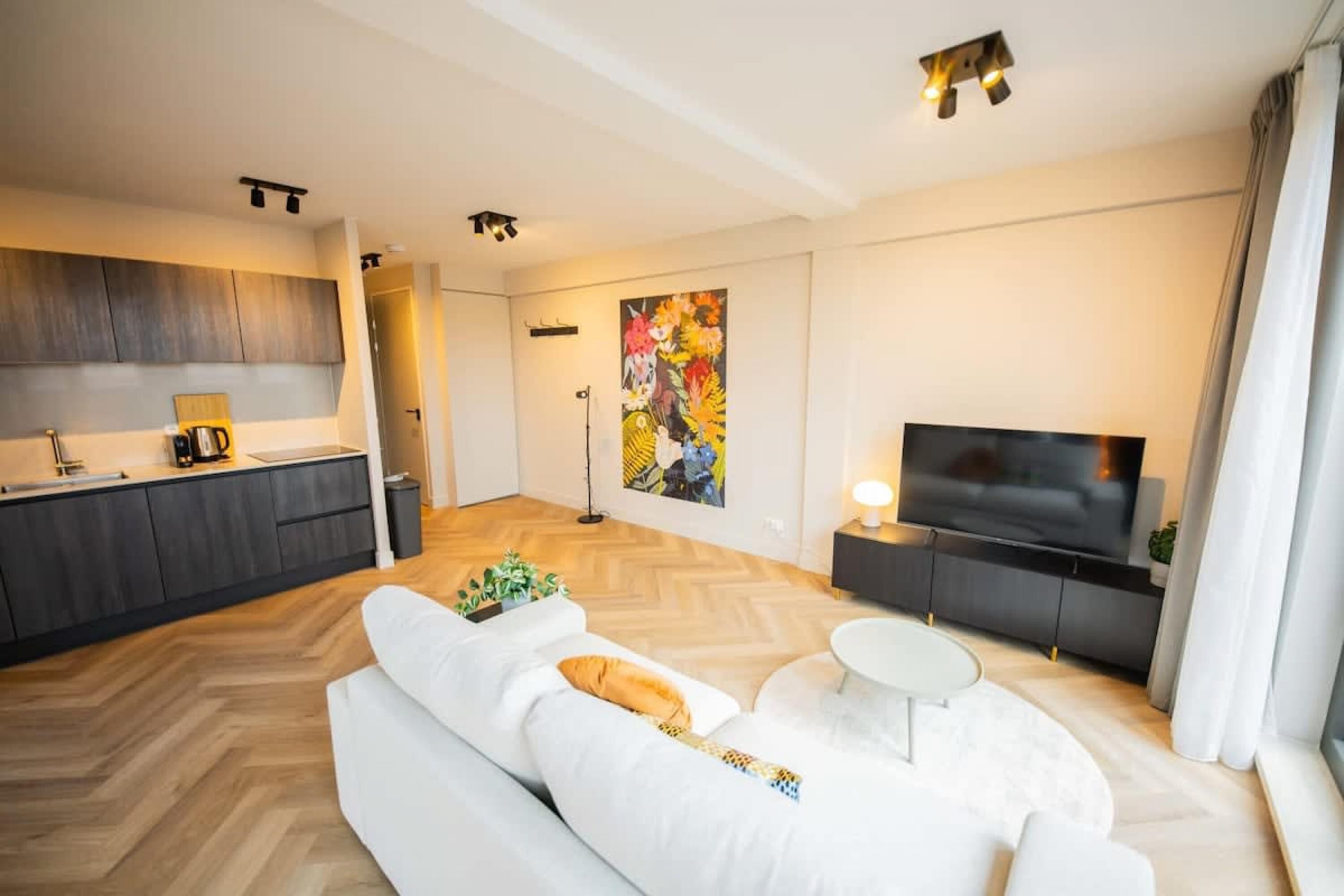 A modern living room with a sofa, a coffee table, a TV, and a kitchen area in the background.