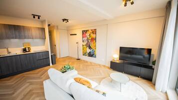 A modern living room with a sofa, a coffee table, a TV, and a kitchen area in the background.