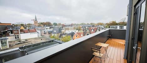 A rooftop terrace with a wooden deck, a table, and chairs.