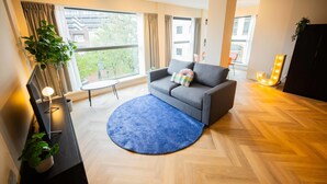 A modern living room with a grey sofa, a blue rug, and a potted plant. - Joyful Serviced Studio Apartment -ks71-j (Hilversum)