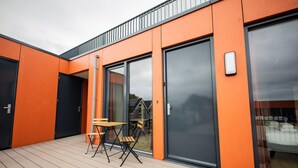 A modern building with orange exterior walls, large sliding glass doors, and a wooden deck with outdoor furniture. - Alphabet 3 Bedroom Serviced Apartment -pk- (Rotterdam)