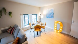 A modern living room with a grey sofa, a dining table with chairs, and a large illuminated 'D' sign. - Alphabet 3 Bedroom Serviced Apartment -pk- (Rotterdam)