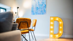 A modern room with a wooden floor, two chairs, a table, and a large illuminated letter 'D'. - Alphabet 3 Bedroom Serviced Apartment -pk- (Rotterdam)
