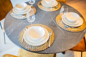 A table set with white plates, bowls, and cutlery, accompanied by woven placemats and wine glasses.