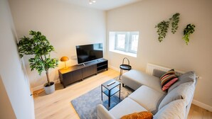 A modern living room with a sofa, a TV, a small table, and a potted plant. - Alphabet 3 Bedroom Serviced Apartment -pk- (Rotterdam)