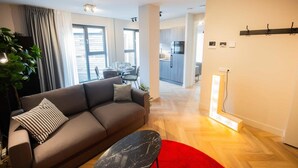 A modern living room with a sofa, a red rug, and a dining area in the background. - Alphabet Apartments 1BR Serviced Apartments (Hilversum)