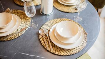 A table set with white plates, cutlery, and glasses on a marble surface with woven placemats.