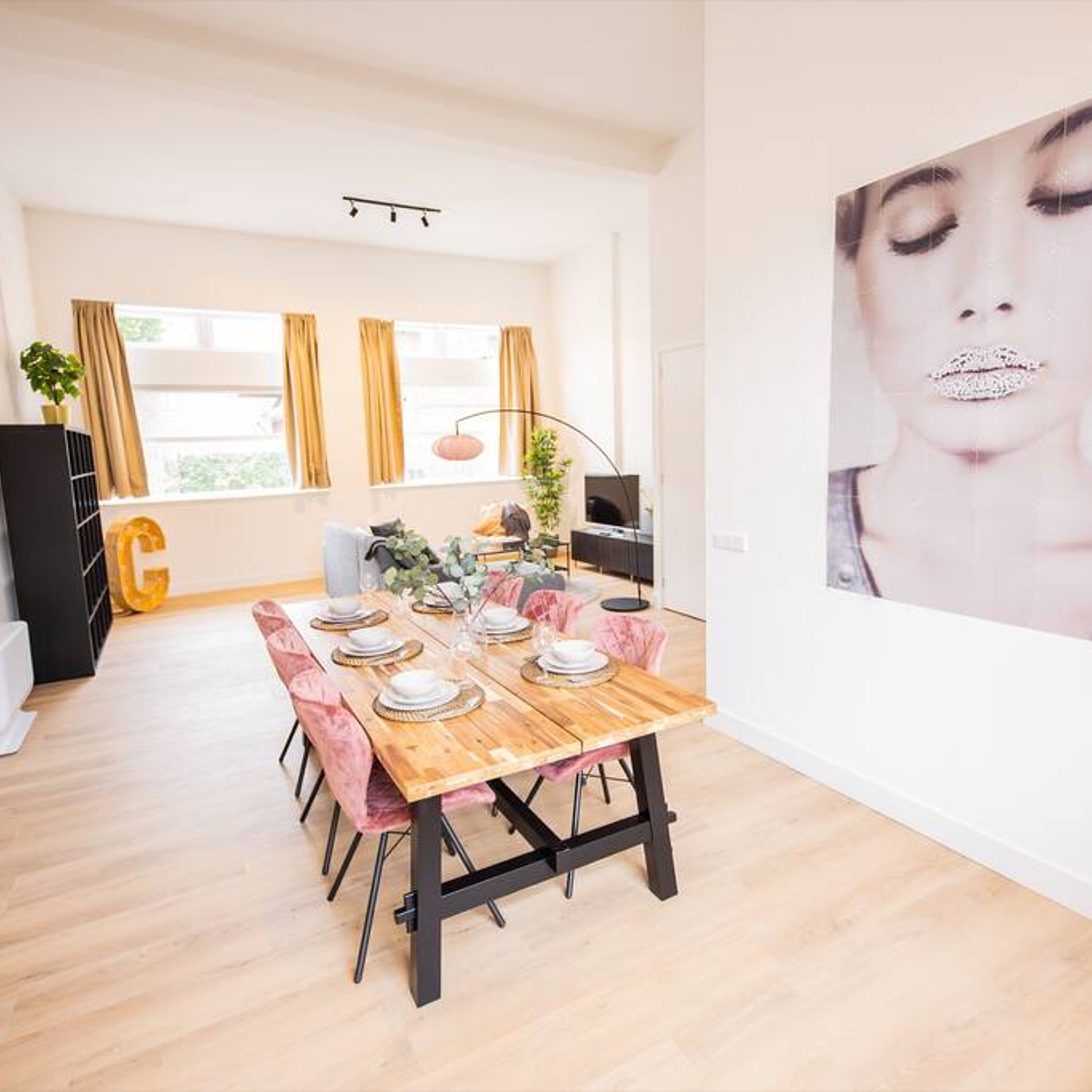 A dining area with a wooden table set for six, surrounded by pink chairs.