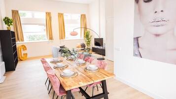 A dining area with a wooden table set for six, surrounded by pink chairs.