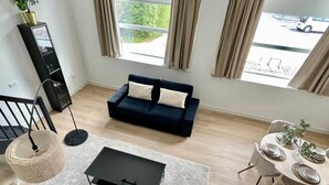 Ein modernes Wohnzimmer mit einem dunkelblauen Sofa, einem kleinen schwarzen Couchtisch und einem Essbereich mit einem weißen Tisch, gedeckt für vier Personen.