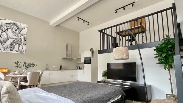 Ein modernes Schlafzimmer mit Bett, Schreibtisch, Fernseher und einer Treppe.