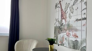 Ein Zimmer mit zwei Sesseln, einem kleinen Tisch mit einer Pflanze und einem großen Wandbild mit tropischer Tierwelt.