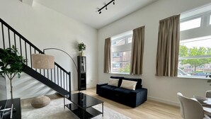 Ein modernes Wohnzimmer mit Treppe, einem schwarzen Sofa, einem Glastisch und einem Essbereich mit einem Stuhl.