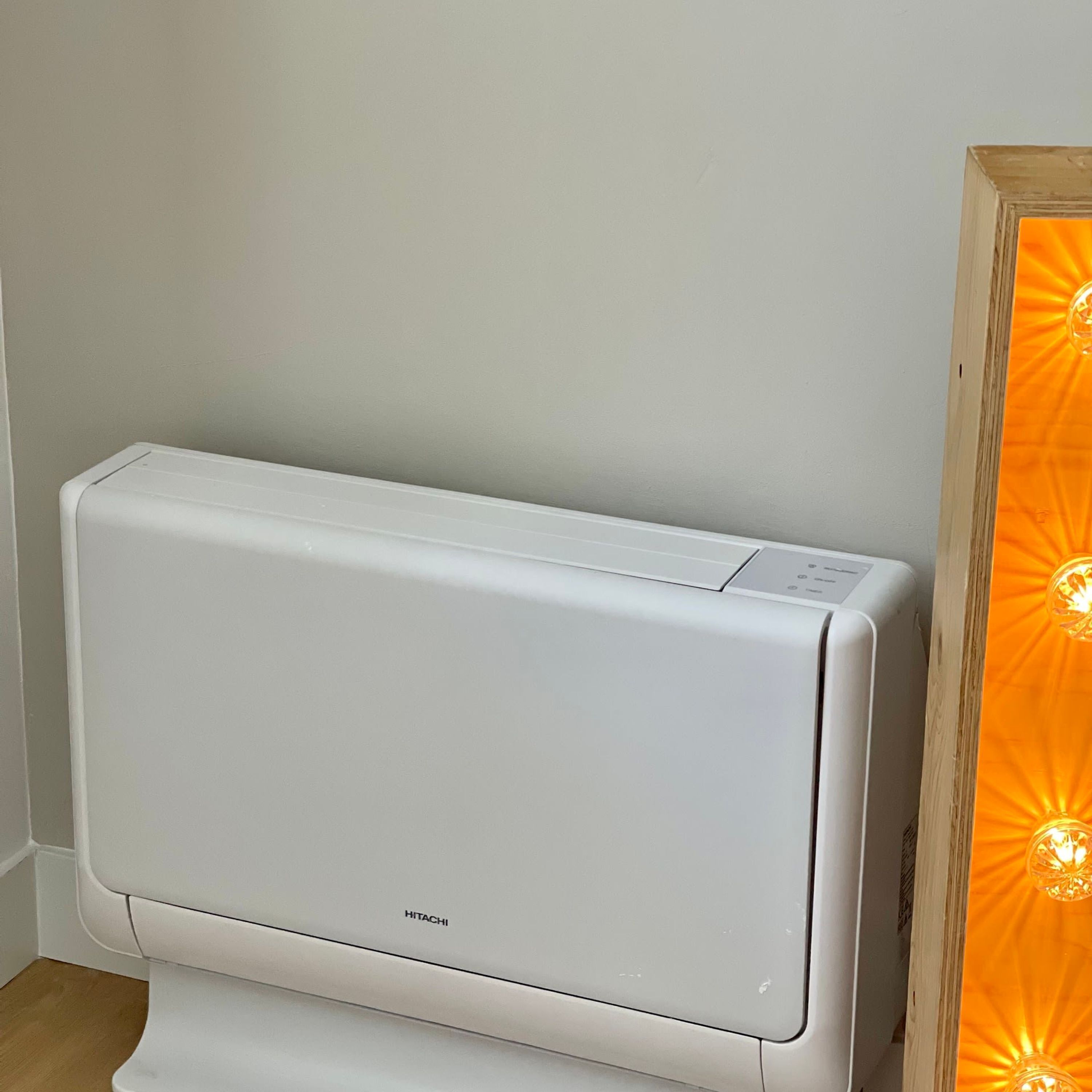 Een Hitachi airconditioner in een ruimte met een houten vloer en een effen muur.