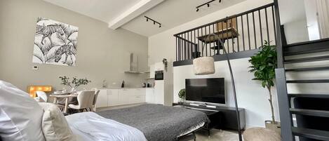 A modern bedroom with a bed, a desk, and a kitchenette.