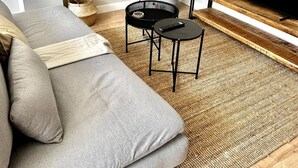 Un salon avec un canapé gris, une petite table noire, un téléviseur posé sur un meuble en bois et une plante en pot.