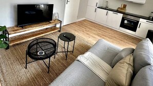 Un salon moderne doté d’un téléviseur à écran plat, d’un canapé, d’une table basse et d’un coin cuisine avec des placards et une cuisinière.