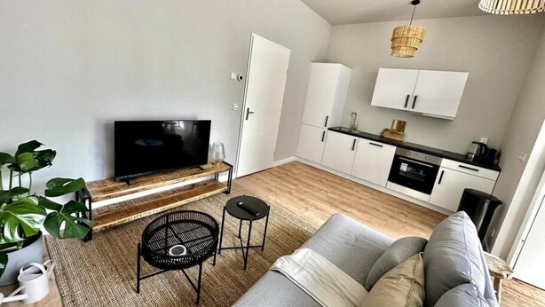 Un salon moderne doté d’un téléviseur à écran plat, d’un canapé, d’une table basse et d’un coin repas avec une cuisine en arrière-plan.