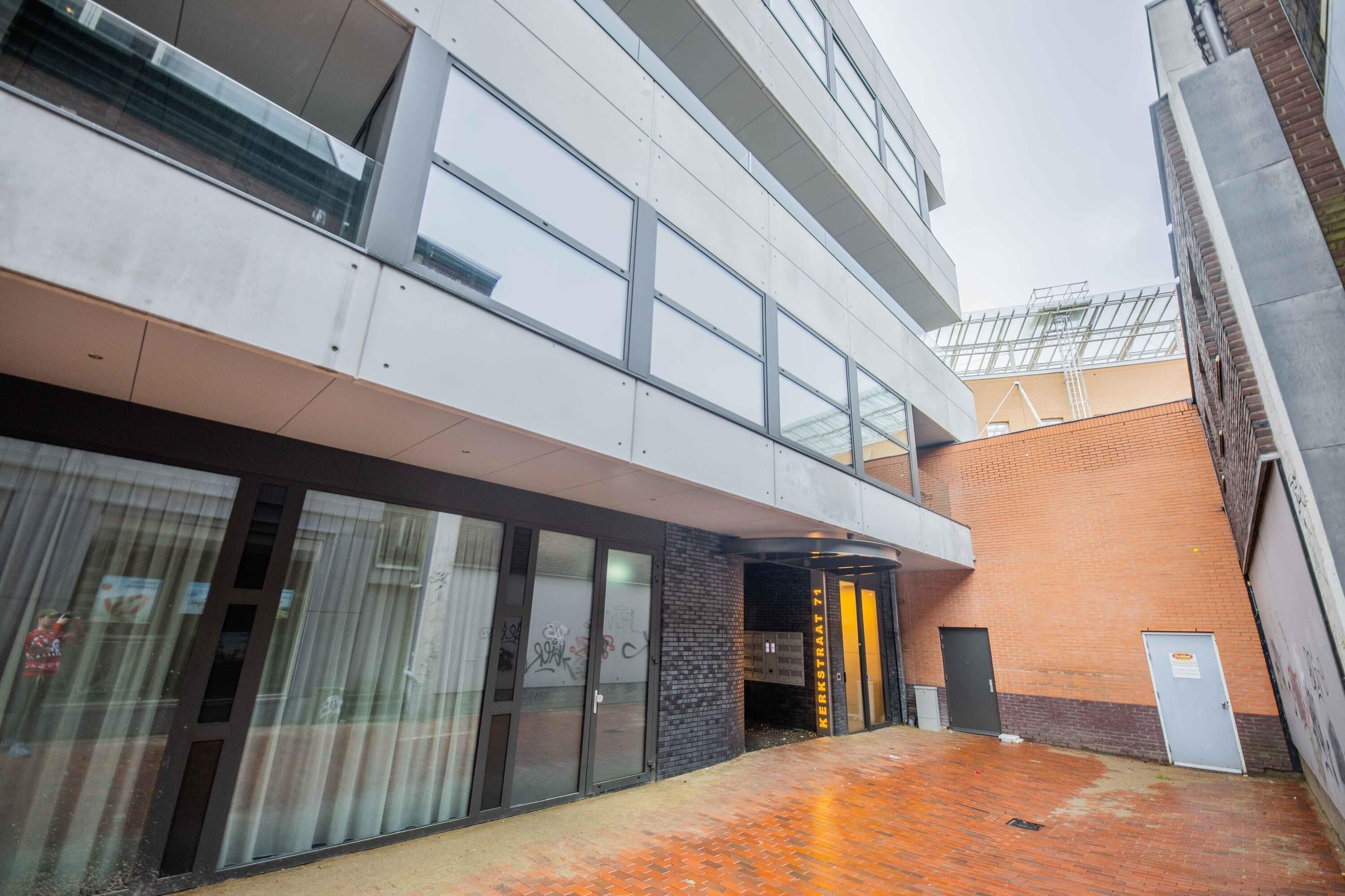 A modern building with a glass facade, a brick lower section, and a metal staircase leading to an entrance.