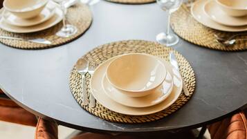 A round table set for four with woven placemats, beige plates, and clear wine glasses.