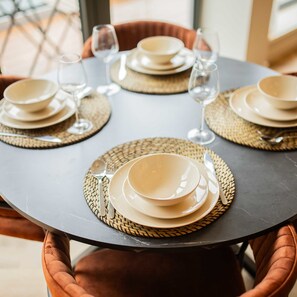 A round table set for four with woven placemats, beige plates, and clear wine glasses. - Studio Serviced Apartments With City View (Hilversum)