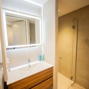 A bathroom with a white sink, wooden vanity, and a glass shower enclosure. - Studio Serviced Apartments With City View (Hilversum)