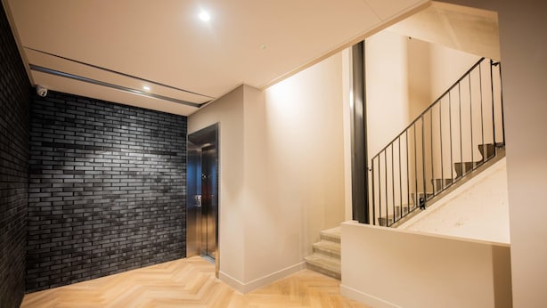 A modern interior with a herringbone wooden floor, a black brick wall, and a staircase with metal railings. - Studio Serviced Apartments With City View (Hilversum)