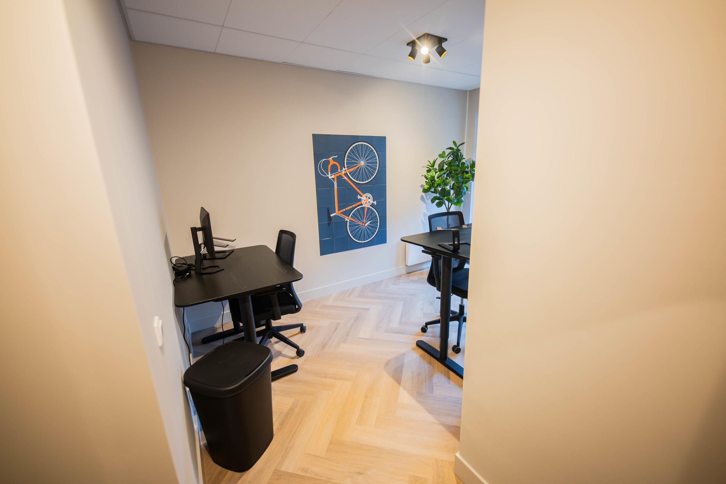 A modern office space with two desks, chairs, and a black trash bin.