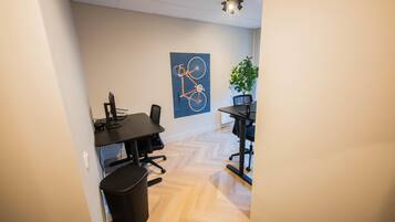 A modern office space with two desks, chairs, and a black trash bin.