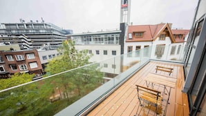 A balcony with wooden flooring and metal railings, overlooking a cityscape with various buildings and a tree. - Studio Serviced Apartments With City View (Hilversum)