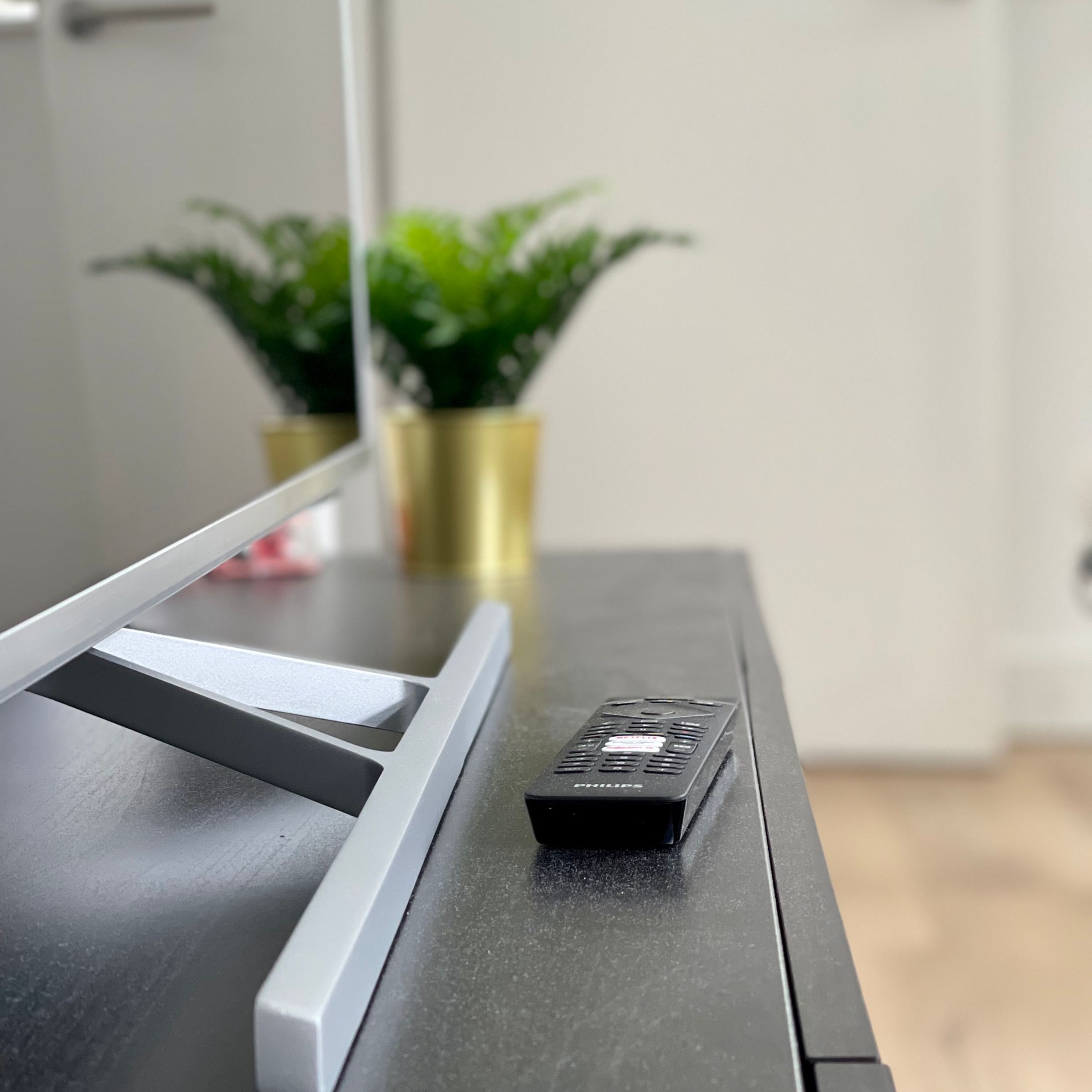 Una TV a schermo piatto su un supporto nero con un telecomando accanto.