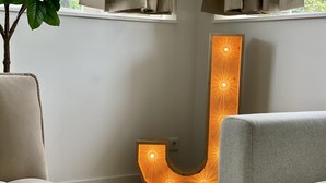 A modern interior with a large illuminated letter 'L' sculpture, a wooden floor, and a window with curtains. - Serviced Studio Apartments in Utrecht (De Bilt)