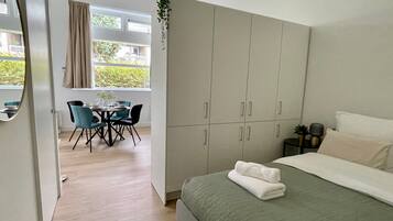 A modern bedroom with a bed, a desk with chairs, and a view of the outside.