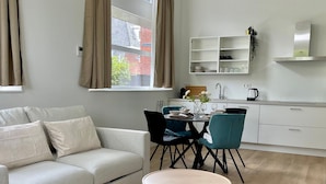 A modern living room with a sofa, a round coffee table, and a dining area with chairs and a table. - Serviced Studio Apartments in Utrecht (De Bilt)