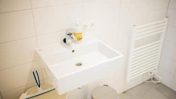 A bathroom with a white sink, a hand soap dispenser, a towel rack, and a waste bin.