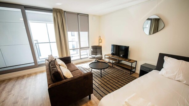 A hotel room with a large bed, a sofa, a TV, a small table, and a window with curtains. - Studio Serviced Apartments With View -prh14/15- (Rotterdam)